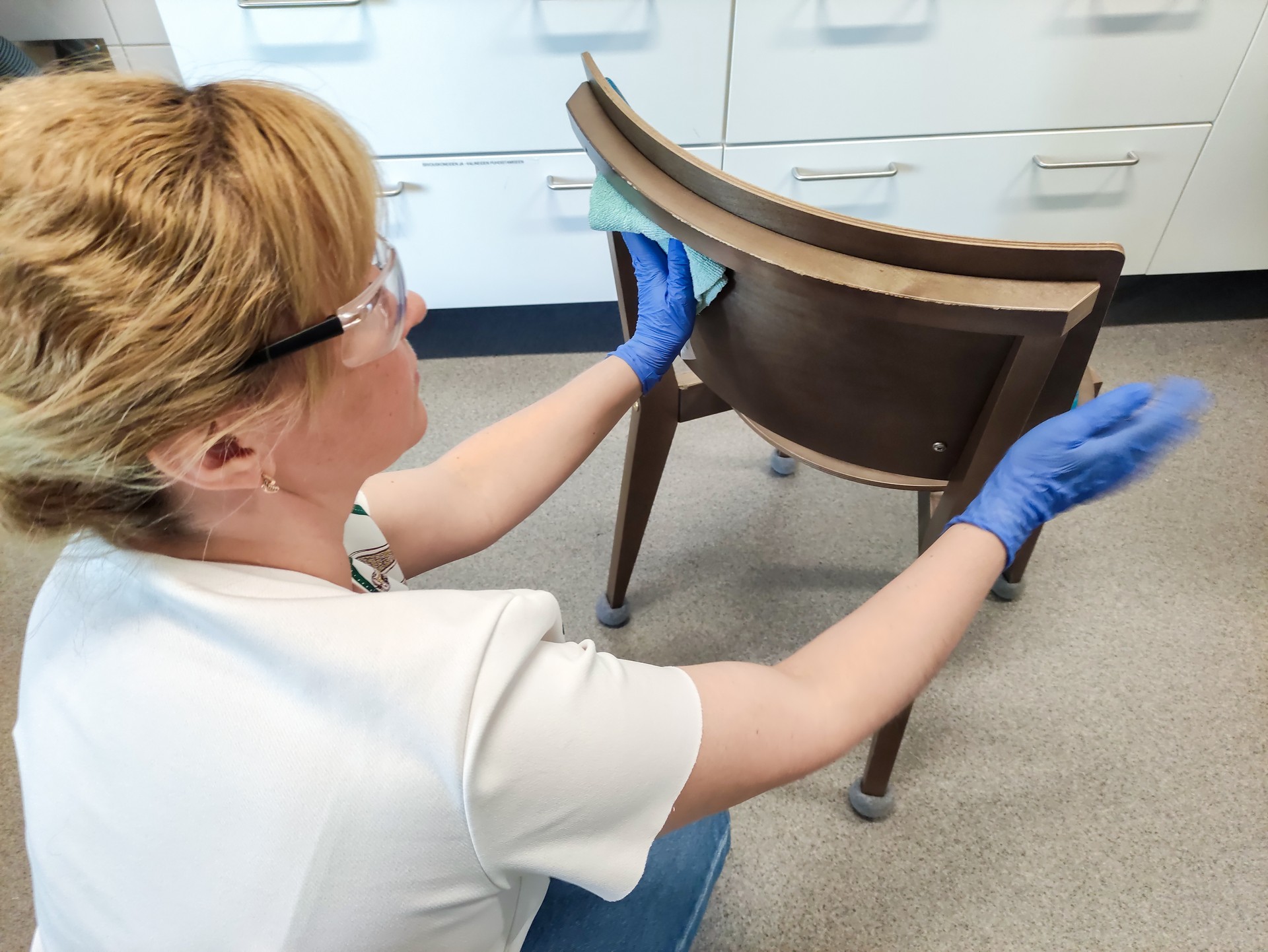 A young woman cleans a chair, wipes it with a cleaning cloth and cleaning product.